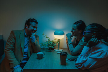 Three colleagues laughing in the office cafeteria and talking during nighttime