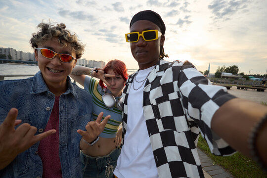 Portrait of diverse group of teenagers posing for selfie outdoors, smiling and gesturing with hands, multiethnic friends including Caucasian, Black boy, girl enjoying time together