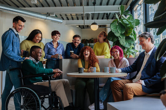 Diverse business team enjoying coffee break, laughing together in modern office - Powered by Adobe