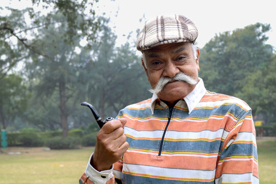 Portrait of a Indian happy senior man standing with holding cheroot pipe at outdoor park. Indian old man freedom and travel after retirement and happiness senior citizen lifestyle