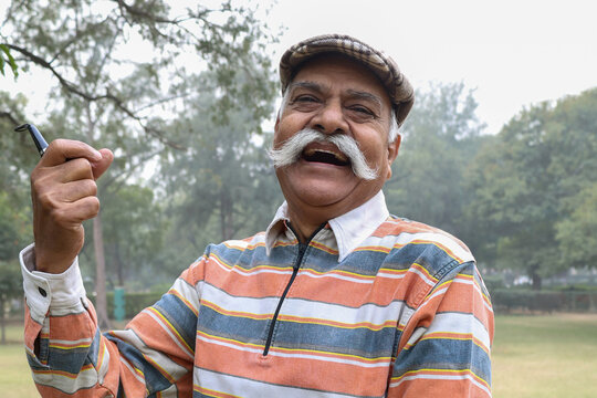 Portrait of a Indian happy senior man standing with holding cheroot pipe at outdoor park. Indian old man freedom and travel after retirement and happiness senior citizen lifestyle