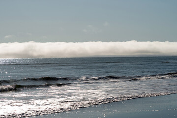 Sunlight reflects off rolling ocean waves as a dense fog bank drifts across the horizon, creating a luminous contrast of water, sky, and mist. Sea of Okhotsk, Sakhalin Island