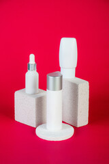 Cosmetic product in tube, bottle, lotion or serum with stylish props on red background. 