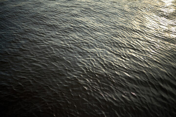 Surface of rippling water reflecting sunlight, creating textured pattern across entire frame, natural outdoor scene showing gentle movement and shimmering highlights on water