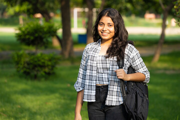 Indian young female college girl student in casual clothes  holding her exams notepad and and backpack while walking in the campus park. Concept of Girl education