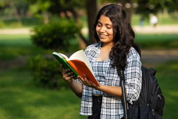 Indian young female college girl student in casual clothes  holding her exams notepad and and backpack while walking in the campus park. Concept of Girl education