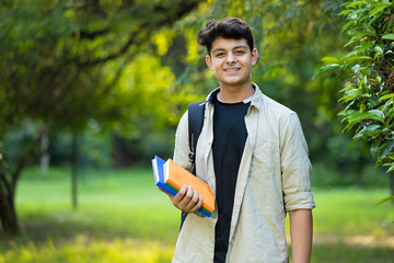 Portrait of indian college boy holding books with with smiling standing in the park. Asian educational student concepts