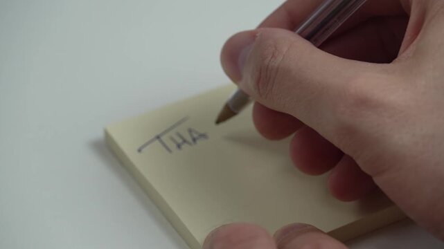 Man hand writing THANK YOU on yellow sticky note.Close-up video of a man's hand writing the words "THANK YOU" on a yellow post-it note. Concept of gratitude, appreciation, communication