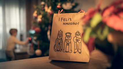 Bolsa de navidad de papel con reyes magos dibujados y niño desenfocado de fondo © Daniel Arsenio