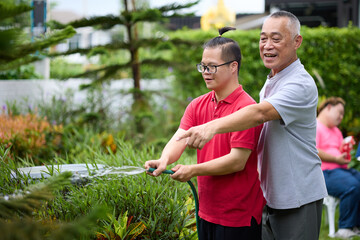 A happy moment of a senior man and a young man with down syndrome holding a water hose in a garden, enjoying outdoor activity together