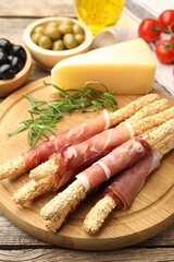 Delicious grissini sticks with sesame seeds, prosciutto and other products on wooden table, closeup
