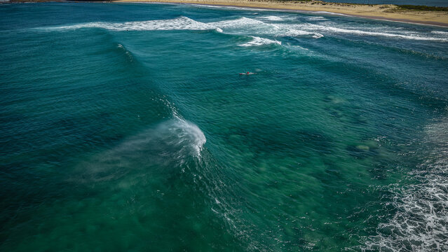 Aerial view of the turquoise waves crashing onto the sandy beach, creating a mesmerizing dance of light and shadow where the ocean meets the shore, Newcastle, New South Wales, Australia.