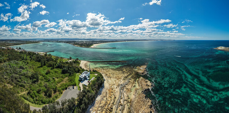 Aerial view of vibrant turquoise waters meet rocky shores and lush green headlands, revealing the scenic beauty of the coast, Swansea, New South Wales, Australia.