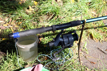 Close-up of black and blue fishing rod with spinning reel resting on green grass, next to plastic...