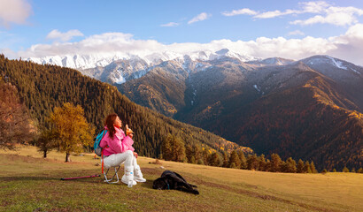 Asian woman as her dog rest and enjoy of the view as sitting on a chair. Hiking in nature. in Mestia Mountain ,Georgia