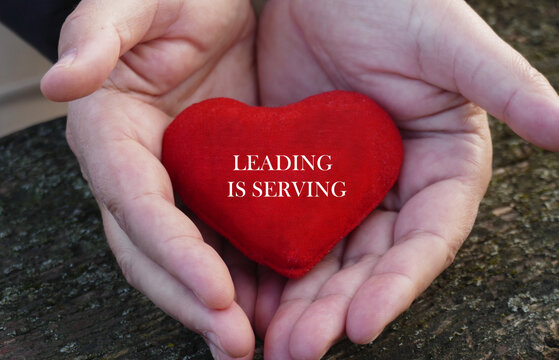 Leading is serving - man hold in hands a red heart with motivational text