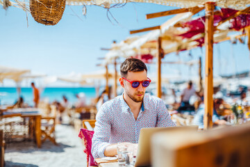 Young caucasian male freelancer working on laptop at seaside beach cafe