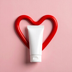White cosmetic tube red heart shape flat lay pink background simple and striking concept love beauty skincare minimal emotional expression of care