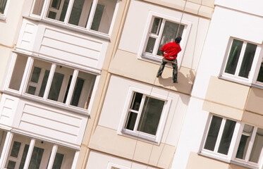 Worker repairs building exterior while rappelling down side of high-rise apartment