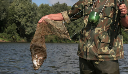 Naklejka premium Fisherman standing by river holding net with caught fish during sunny day