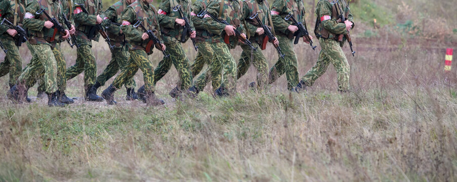 Soldiers march in formation across a grassy field during military training exercises in an outdoor setting - Powered by Adobe