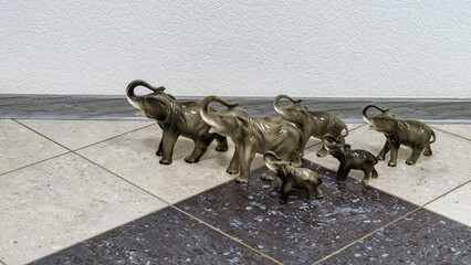 Group of porcelain elephant figurines of varying sizes, arranged on tiled floor with textured wall in the background