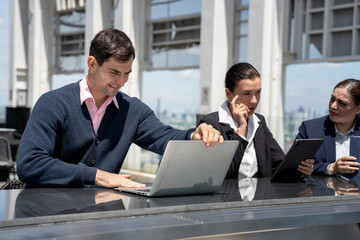 Business team working together on a laptop at outdoor or rooftop office with city background 