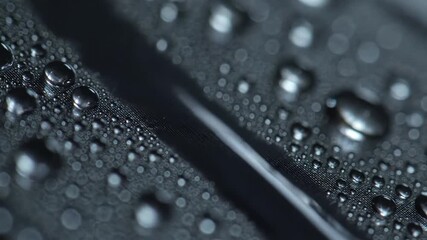 Extreme close up macro shot of water droplets condensing and flowing on a dark metallic hydrophobic surface creating a beautiful abstract background with shallow depth of field.