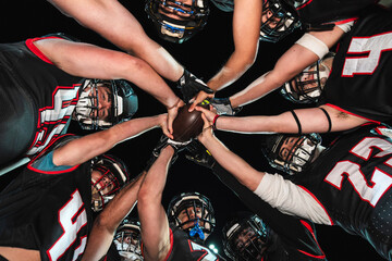American football players putting hands together, holding a ball in a team huddle, showing unity and game preparation © Koldo_Studio