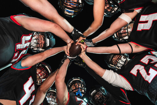 American football players putting hands together, holding a ball in a team huddle, showing unity and game preparation
