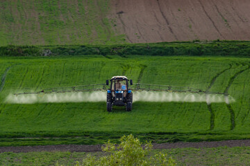 Aerial view of tractor spraying crop in green farm fields with pesticide