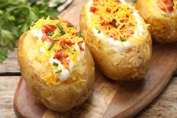 Tasty baked potatoes with sour cream, green onion, cheese and bacon on wooden table, closeup