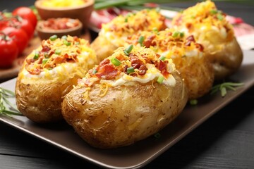 Tasty stuffed baked potatoes on black wooden table, closeup