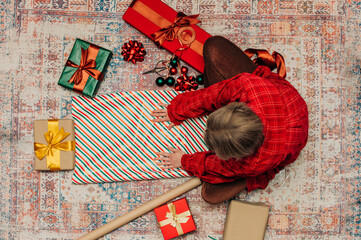 woman sits on a cozy rug surrounded gift boxes, wrapping Christmas presents