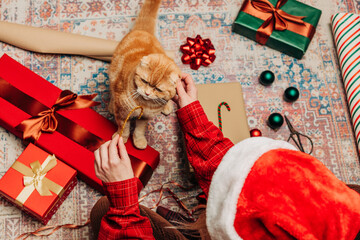 woman sits on cozy rug with boxes, busily wrapping Christmas presents, near ginger cat