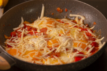Cheesy eggs cooked with vibrant and colorful peppers are sizzling happily in a warm skillet, creating a delicious aroma