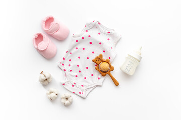 Flat lay of baby accessories - bodysuit and booties with wooden teether toys and bottle of milk on white background, top view