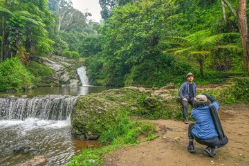 Photographer Capturing Traveler Posing By Stunning Lush Waterfall