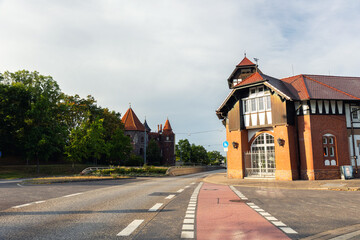 Obraz premium Schleinufer street view in Magdeburg shows brick building with timber elements road intersection, bathed in warm sunlight. Background rise historic towers and castle walls surrounded by green trees