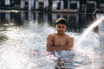 Young man relaxing in resort pool under water jet