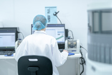 A clinical data scientist in a sterile environment analyzes bioinformatics output on a computer, validating results from a high-throughput automated analyzer connected to the LIS. © ultramansk
