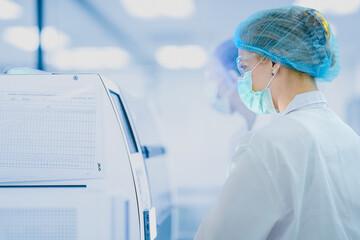 A team of scientists in a sterile laboratory works on a large machine. They are following a checklist to ensure the quality and safety of their medical research or production process.