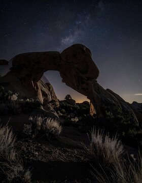 Nighttime archway, starry sky.  Silhouette of a natural rock arch under a Milky Way-streaked sky.  Desert landscape with scrubby vegetation
