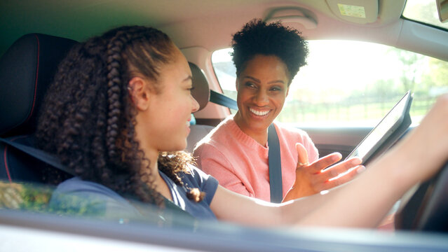 Teenage Girl In Car Having Driving Lesson From Female Instructor Or Parent With Digital Tablet