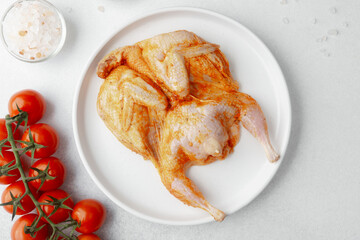 Closeup of marinated raw quail on plate with vine tomatoes and cooking spices