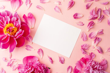 White blank card surrounded by pink peonies and scattered petals on soft pastel background