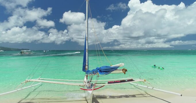 Turquoise tropical water gently lapping the shore of White Beach in Boracay, Philippines, with a traditional paraw sailboat resting on pristine sand under a vibrant blue sky