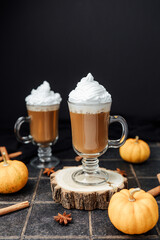Two pumpkin spice lattes with whipped cream and cinnamon sticks on a dark background