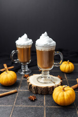 Two pumpkin spice drinks topped with whipped cream, surrounded by mini pumpkins and cinnamon sticks.