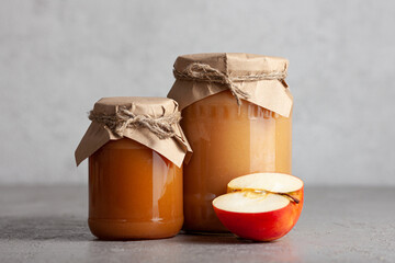 Two jars of apple jam with half an apple on gray background